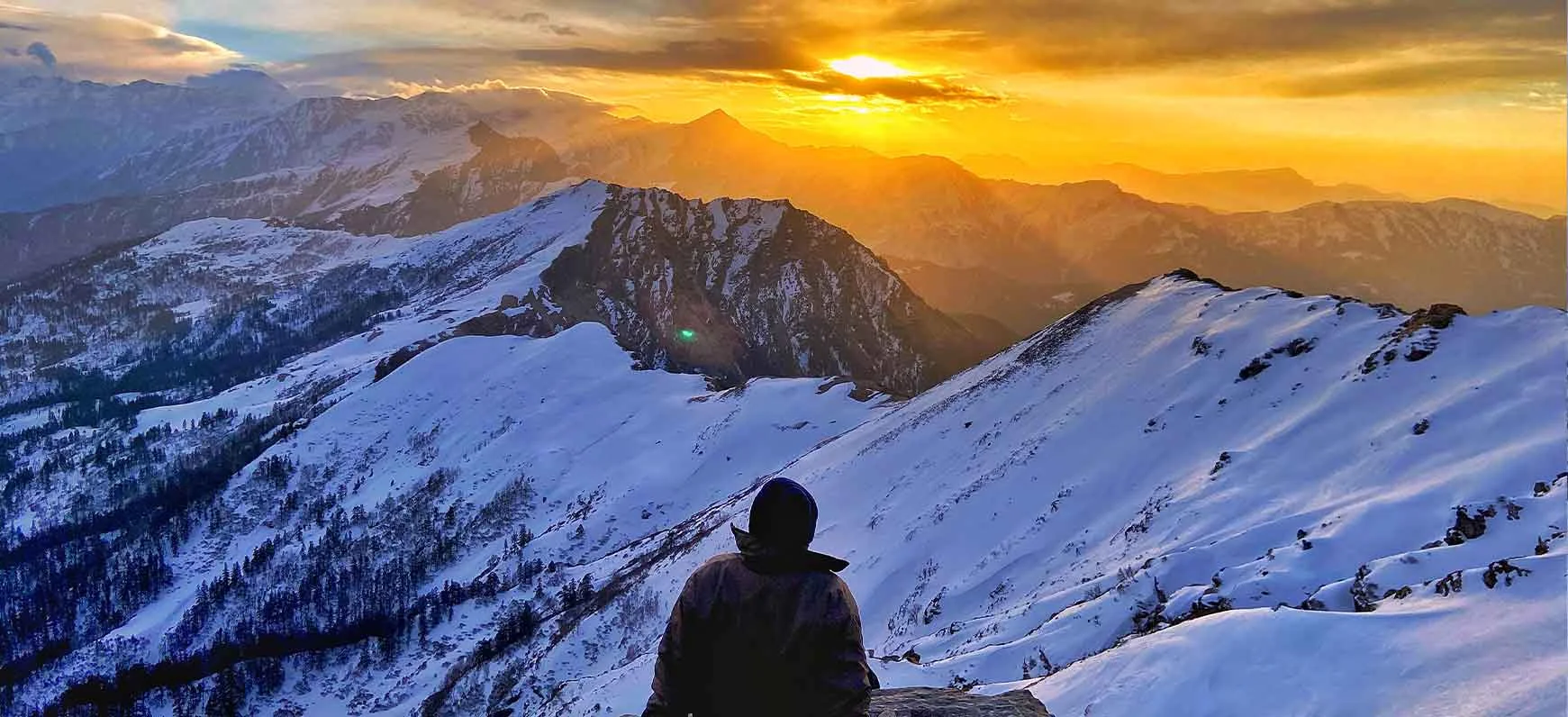 Kedarkantha trek group photo with trekkers posing on a snowy ridge and Himalayan peaks in the background